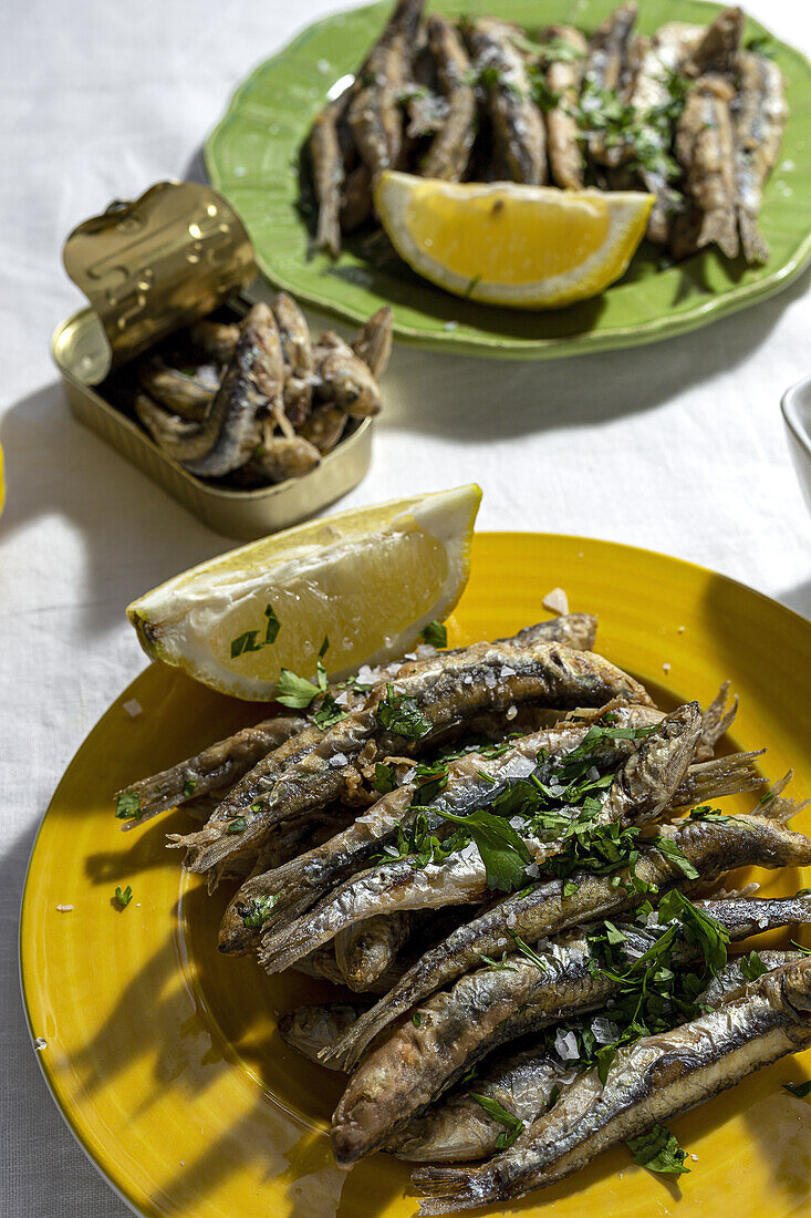 From above plate of appetizing grilled anchovies served on table with piece of lemon and fresh herbs in restaurant