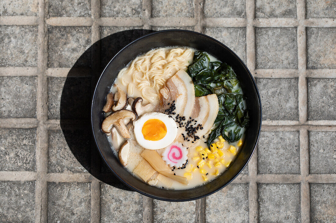 Top view of appetizing Japanese ramen with mushrooms and egg served on paved sidewalk on sunny street in city