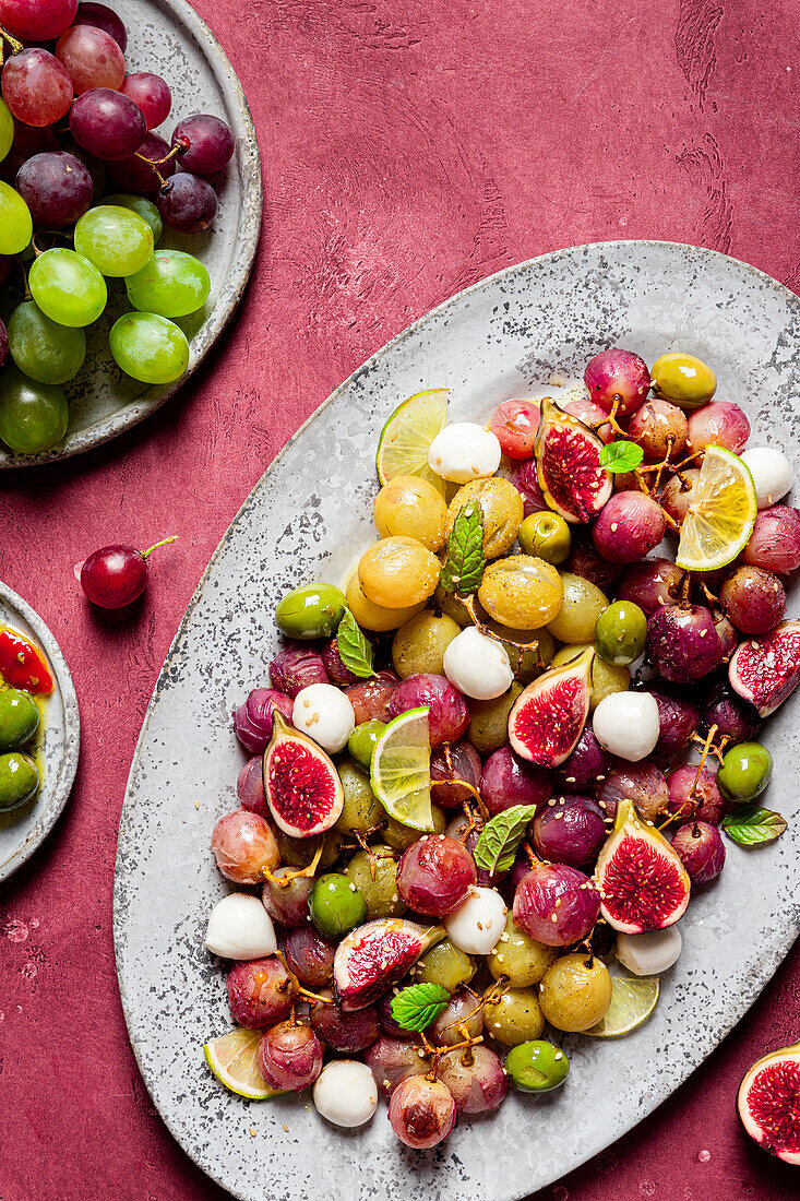 From above fresh ripe grapes, olives, figs and mozzarella seasonal christmas salad placed on plate on red tabletop background