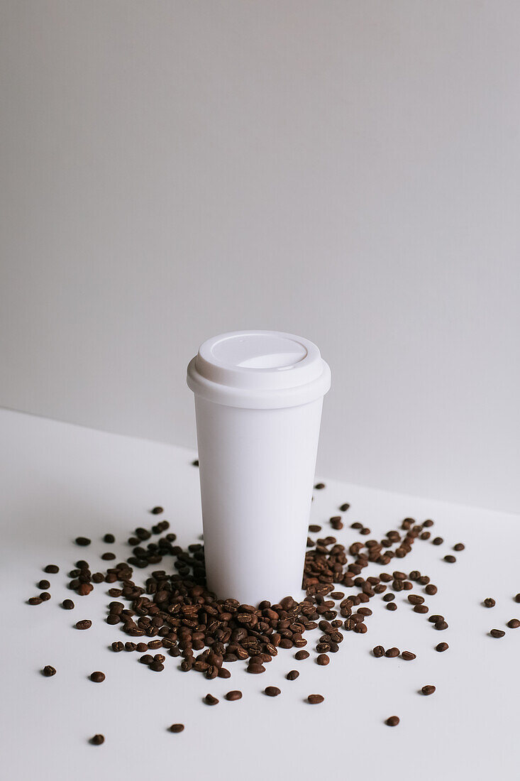 High angle of takeaway paper cup placed on white table with scattered coffee grains in studio