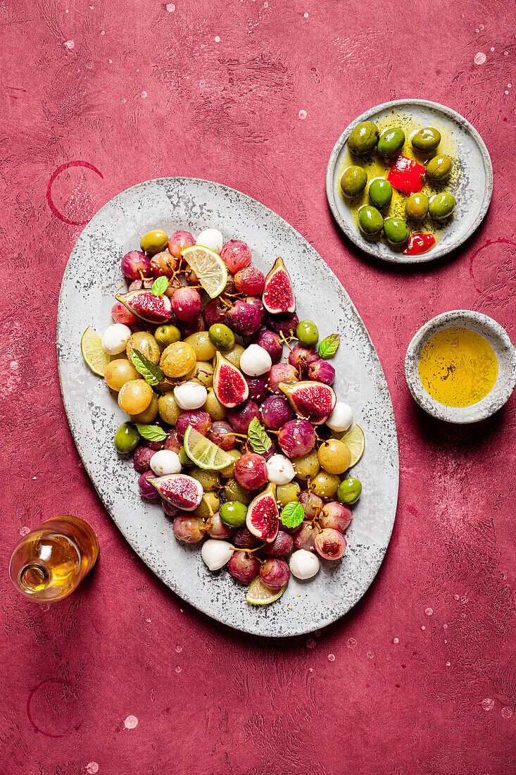 From above fresh ripe grapes, olives, figs and mozzarella seasonal christmas salad placed on plate on red tabletop background