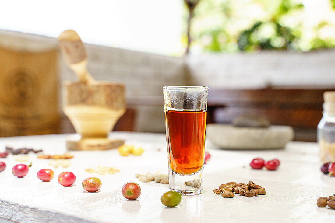 Selective focus of glass of coffee placed on table near row of berries and heap of grains in daylight