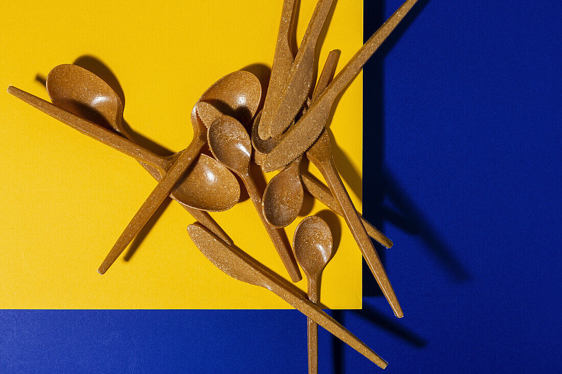 Draufsicht auf braunes umweltfreundliches Besteck vor gelbem und blauem Hintergrund aus Karton