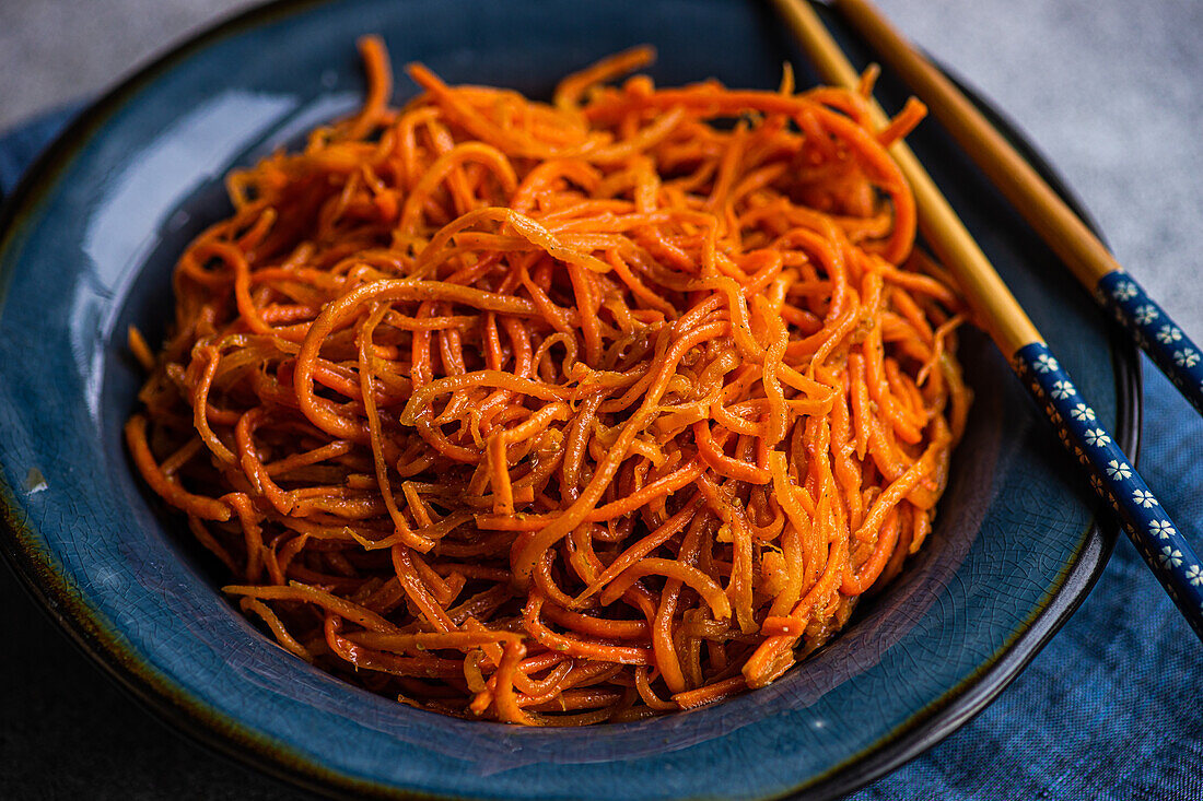 Traditional spicy asian carrot salad served on ceramic plate and chopsticks on concrete background