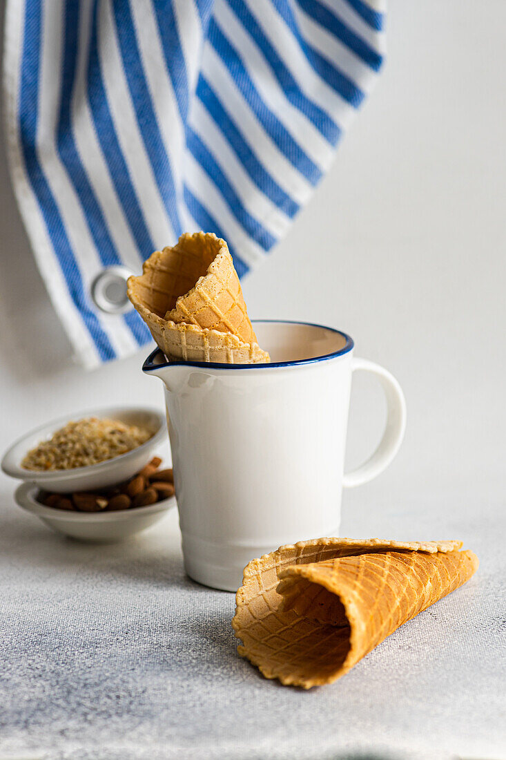 Waffle cones and nuts for ice cream preparation on concrete table with white concrete background with towel