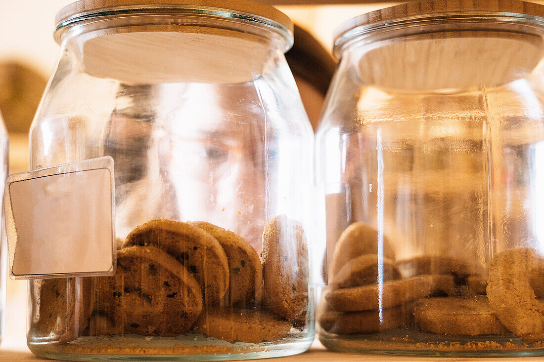 Set of glass jars with chocolate cookies placed on wooden shelf in shop