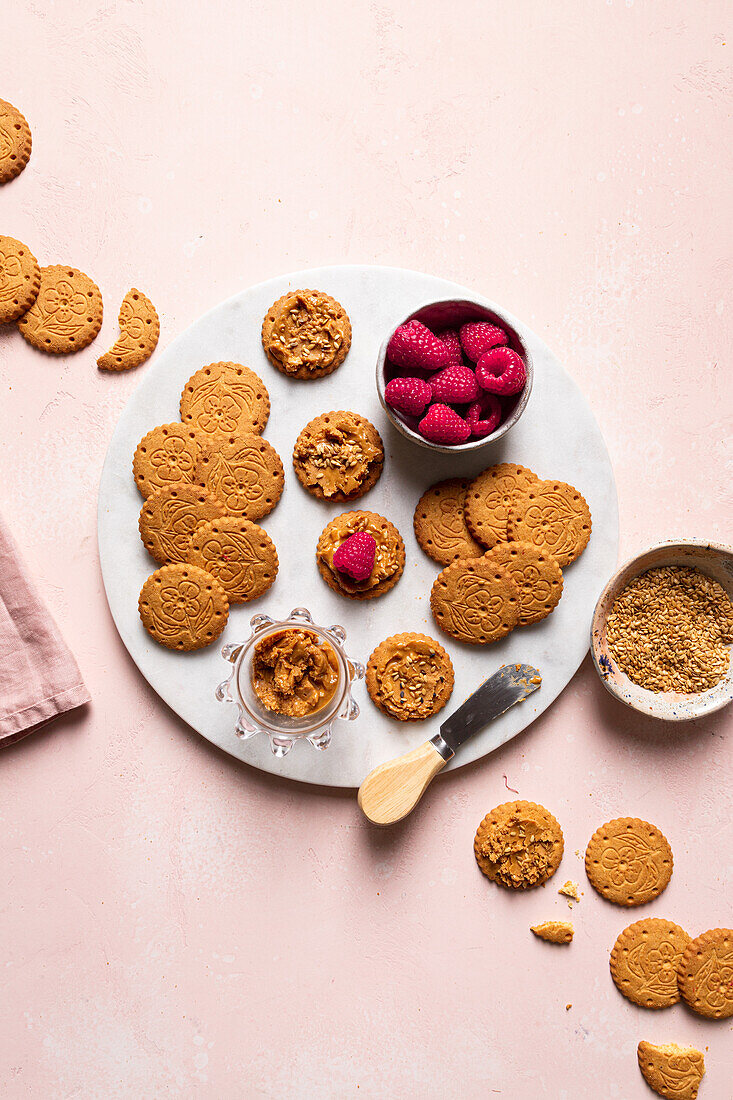 Top view of plates with delicious crispy homemade cookies and fresh raspberries served on table with teapot bowl of seeds