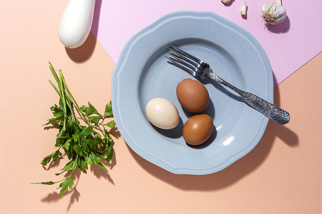 Top view of chicken eggs on plate with fork against fresh parsley sprigs on two color background