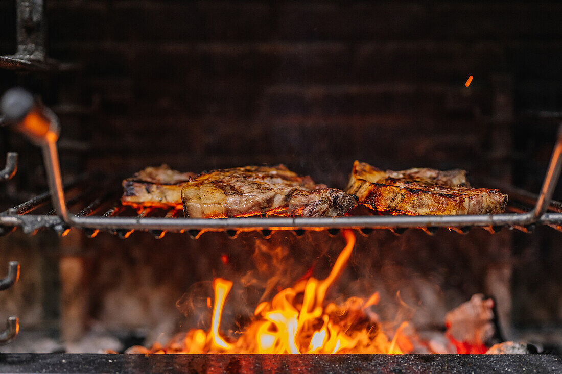 Appetizing juicy steaks placed on barbecue grid over burning flame while frying in grill oven
