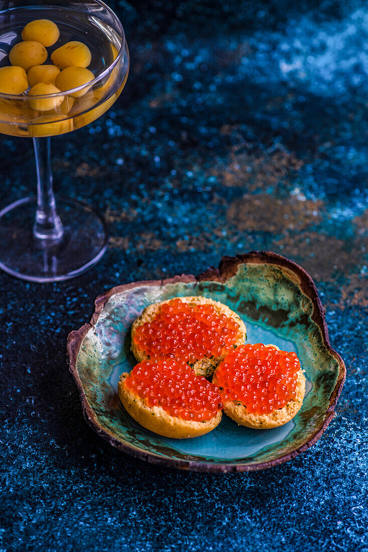 Von oben Bruschetta mit rotem Kaviar auf Keramikteller auf Steintisch neben trockenem Martini im Glas