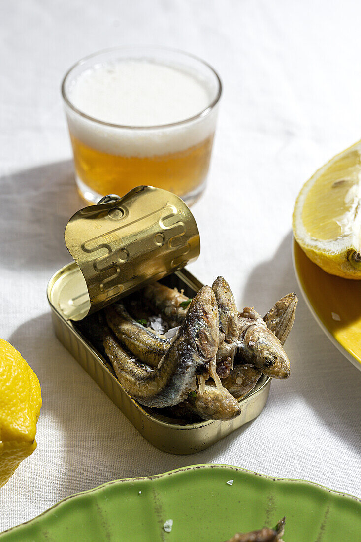 From above of delicious fried anchovies served on can with lemon and placed on white table with glass of beer