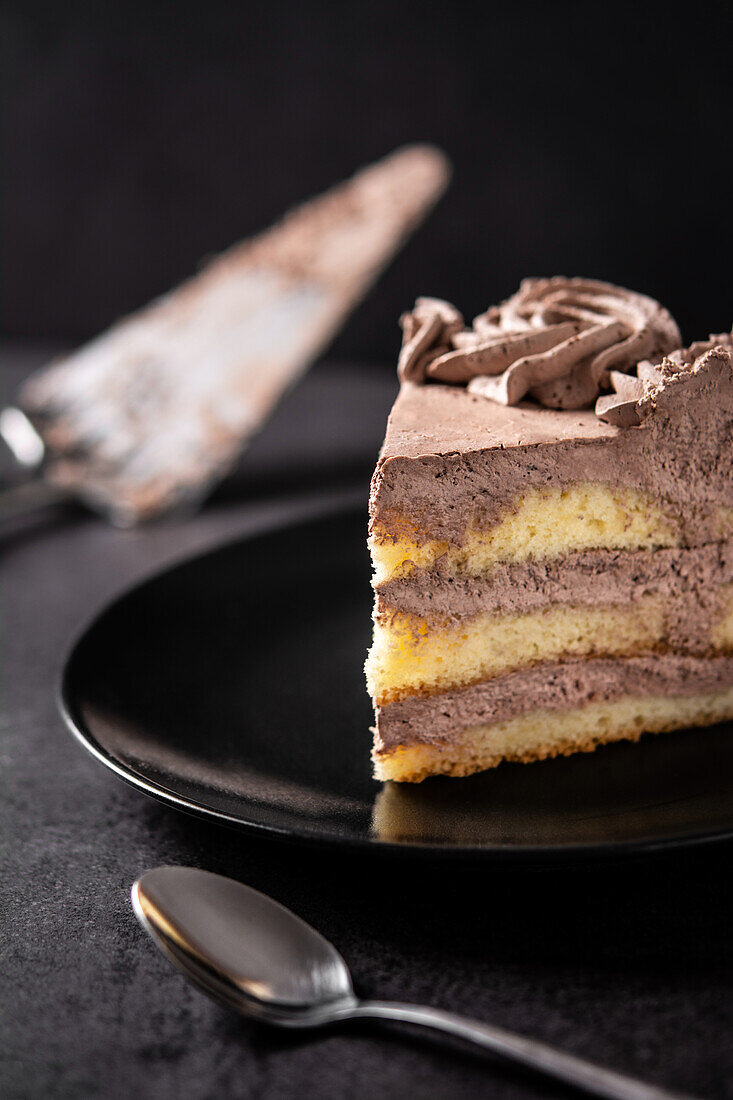Von oben auf ein Stück leckeren Trüffel-Schokoladenkuchen, der in einem Teller auf einem schwarzen Tisch mit Löffel und Spachtel serviert wird