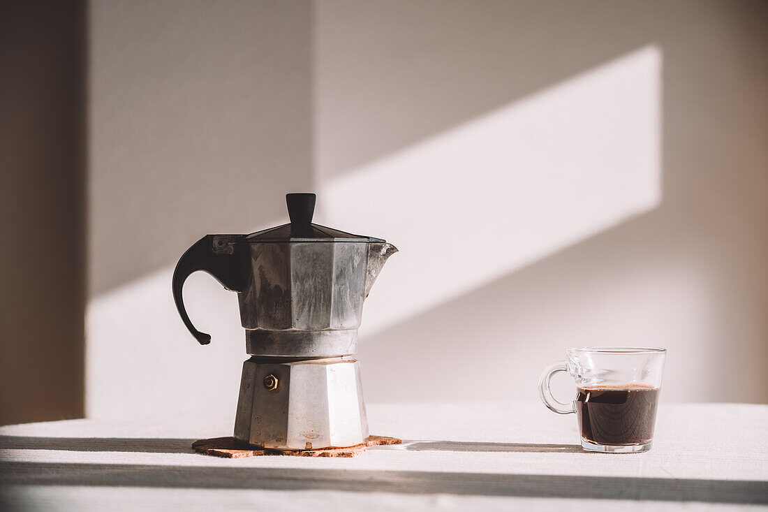 Metallgeysir-Kaffeemaschine auf dem Tisch mit aromatischem Kaffee im irischen Glas in der Küche an einer weißen Wand an einem sonnigen Tag
