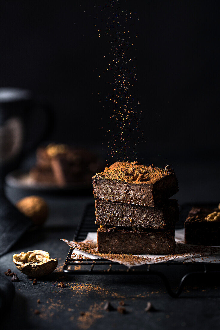 Composition of little stack of tasty sweet brownie cuts with powder on black background