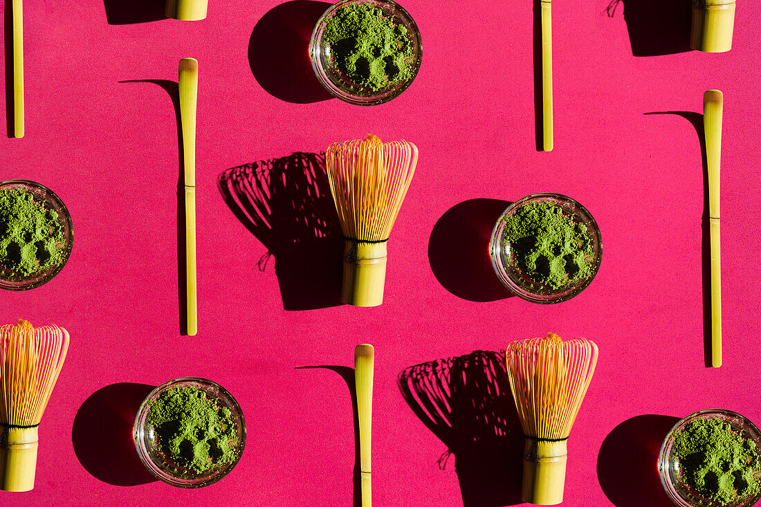 Draufsicht Vollbild heller Hintergrund von Glas mit grünem Tee und getrocknetem Matcha mit Bambus-Chasen und Chashaku auf rosa Oberfläche