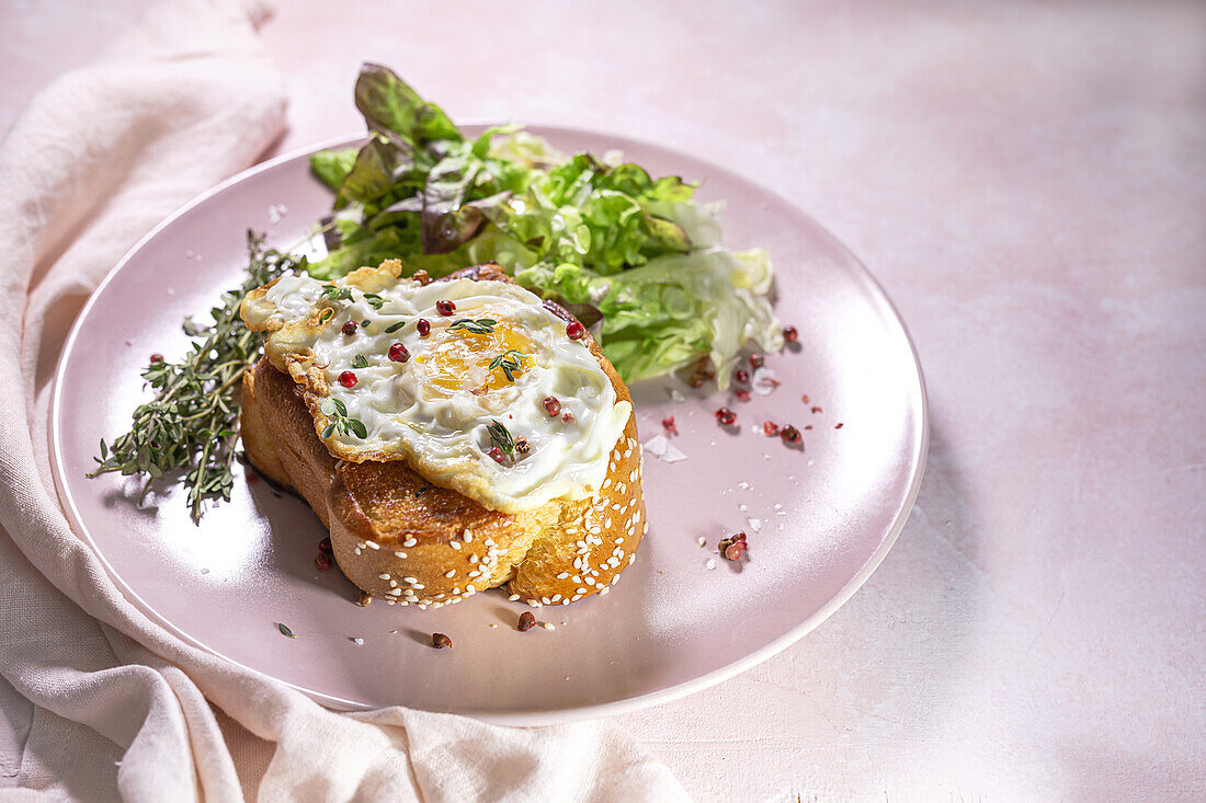 High angle of fried egg on brioche served on plate with fresh lettuce for appetizing breakfast on pink background