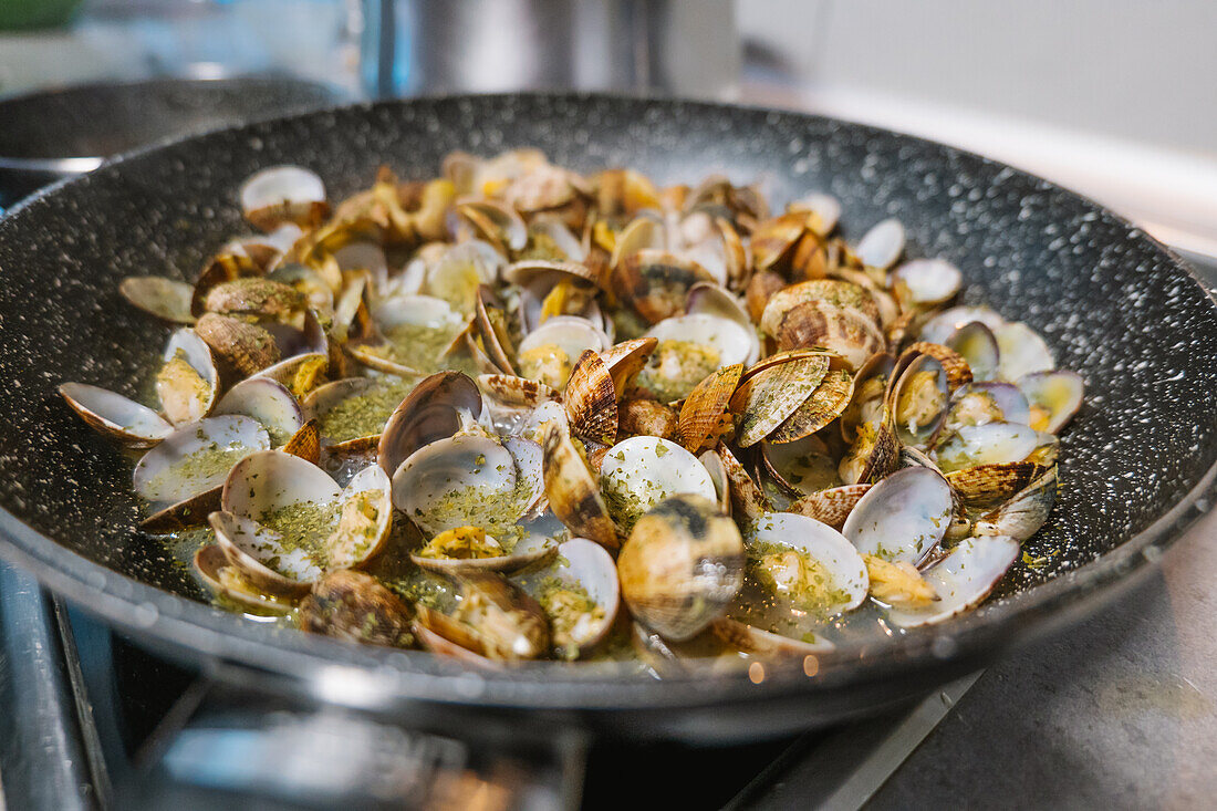 Heap of tasty mollusks with shells frying in hot black frying pan on electric cooker in light kitchen at home