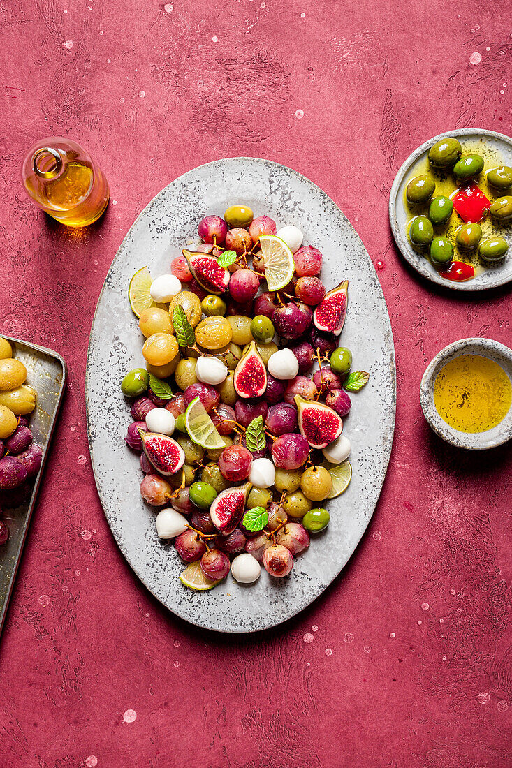 Frische reife Trauben, Oliven, Feigen und Mozzarella auf einem Teller auf rotem Tischhintergrund