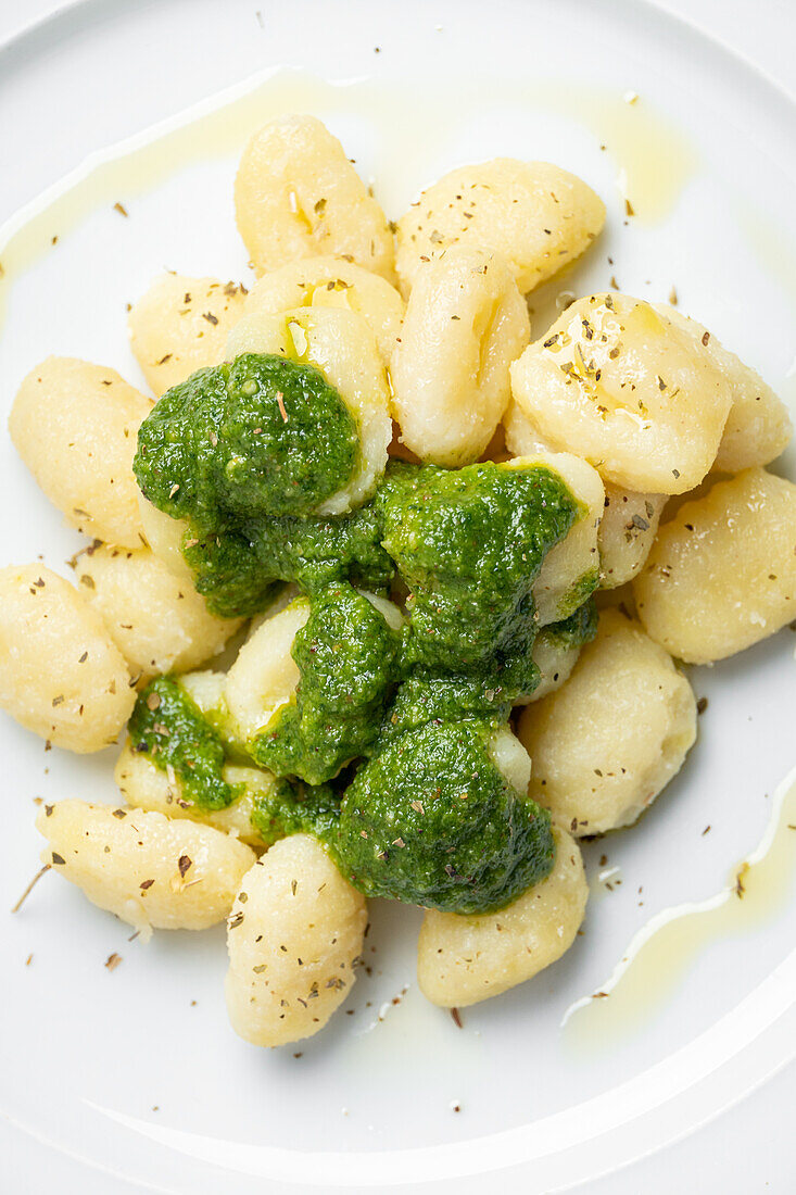 Draufsicht auf appetitliche Gnocchi mit Pesto-Sauce, serviert auf weißem Teller mit Toasts