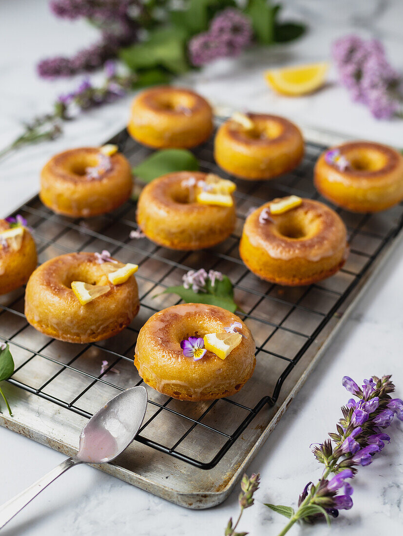Von oben von leckeren Donuts auf Kühlregal mit Blättern zwischen blühenden Lavendelzweigen auf Marmoroberfläche