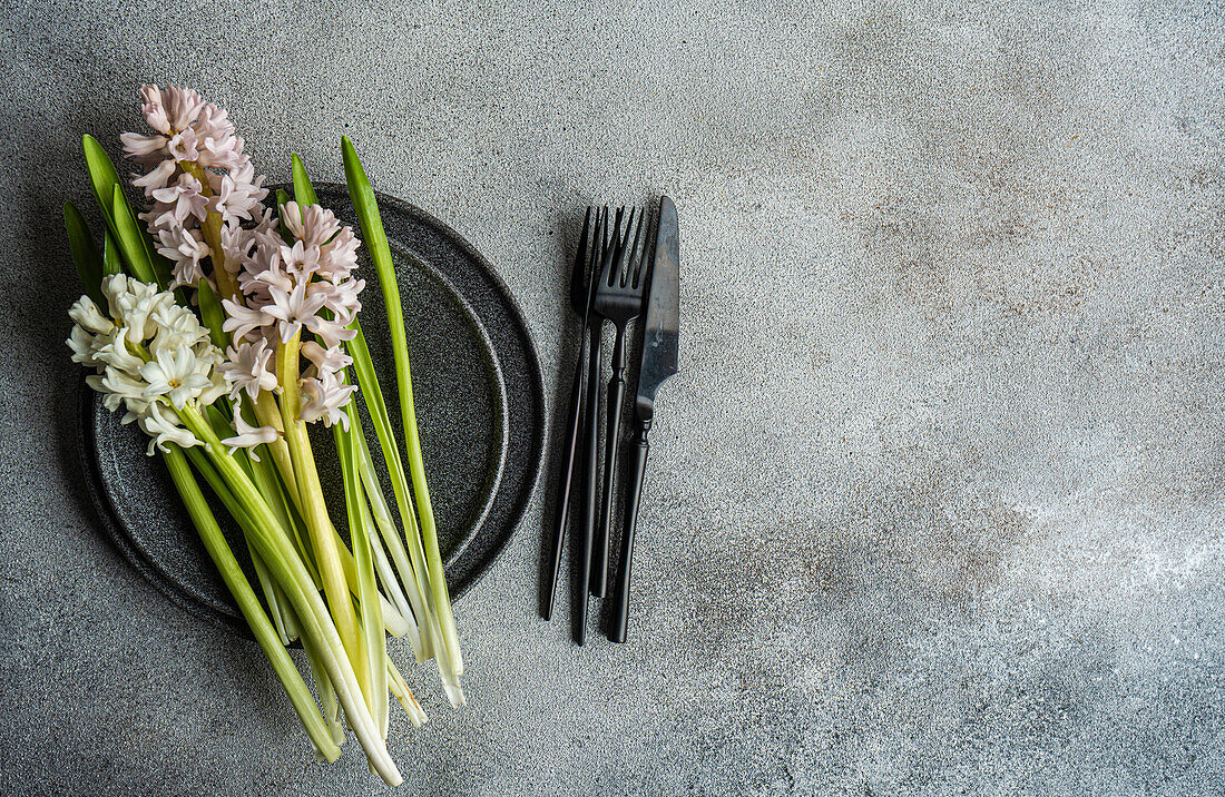 From above spring table setting with hyacinth flower near ceramic plate and cutlery on grey concrete table for festive dinner