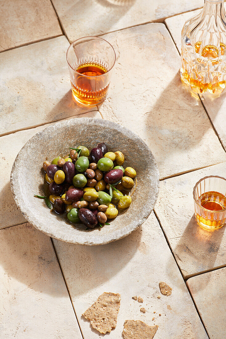 Hoher Winkel von köstlichen Oliven in einer Schale auf einer lebhaften Fliese in der Nähe von Gläsern und einer Glasflasche mit orangefarbenem Alkoholgetränk