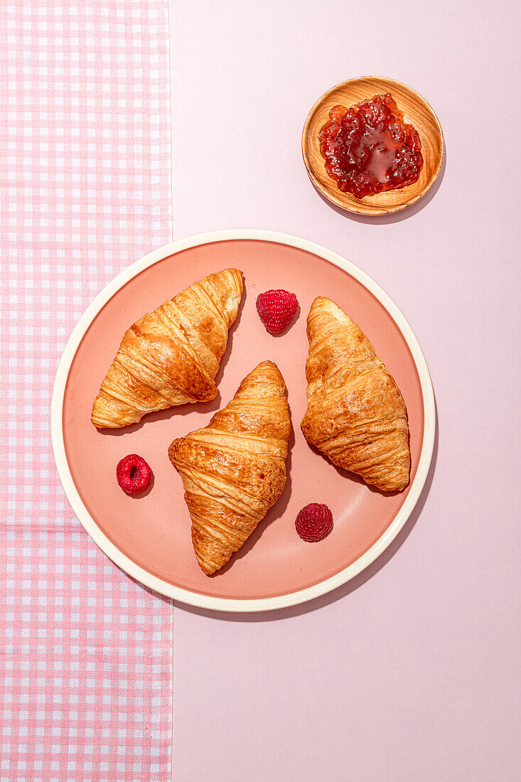 From above of composition of plated with fresh baked sweet croissants served with berries and jam placed on pink table