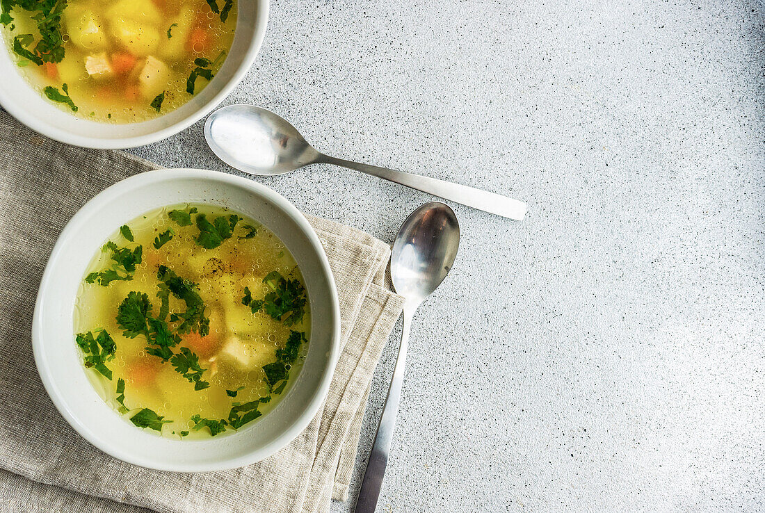 Von oben: Hühnersuppe mit Gemüse in Schalen auf weißem Betontisch, bereit zum Abendessen