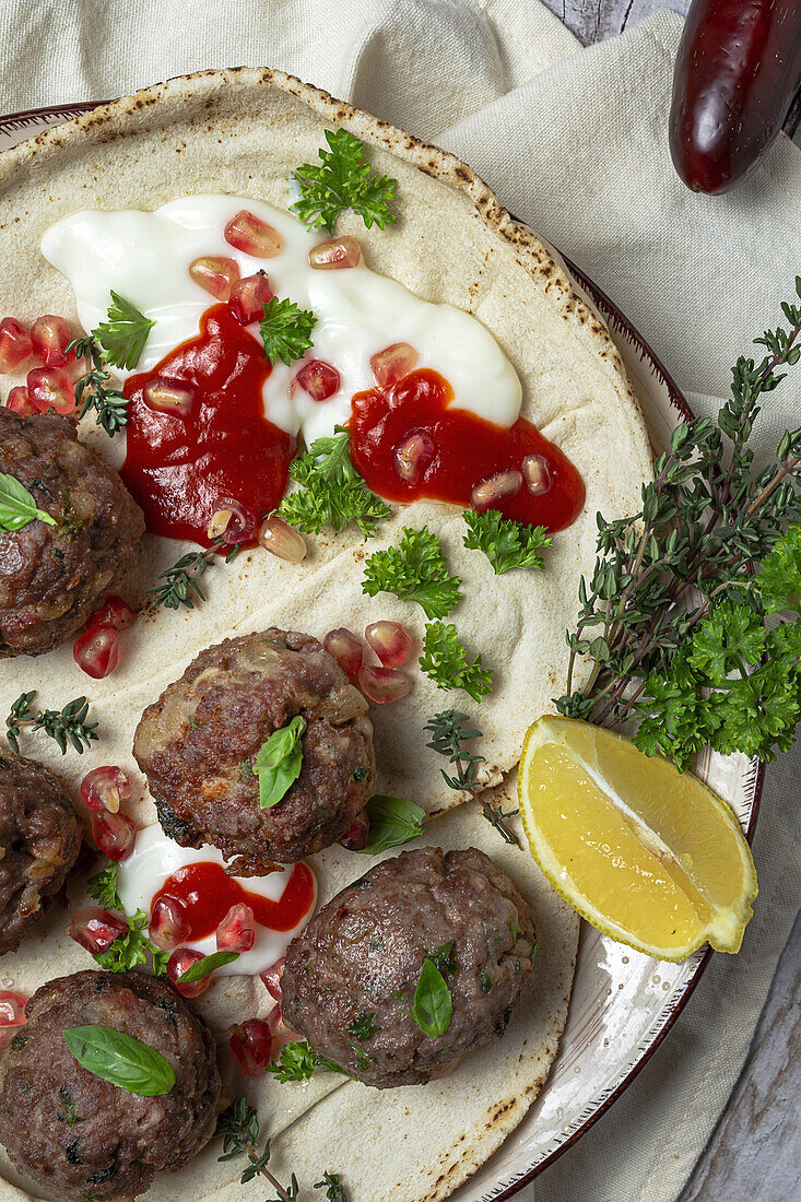 Traditional homemade beef and lamb meatballs with arabic bread, tomato sauce, pomegranate and aromatic herbs. Halal food