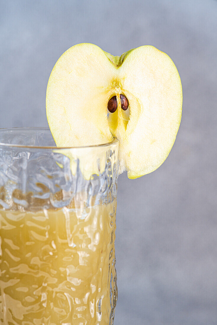 Fresh apple smoothie served in glass with sliced apple on concrete background