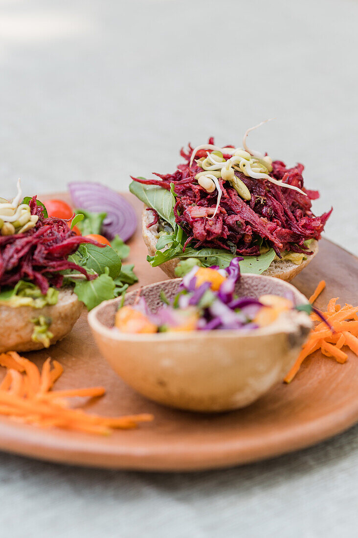 Leckere Sandwiches mit Salat und Roter Bete, serviert mit Gemüse und frischem Salat in einer Schüssel auf einem Holzteller auf einem Tisch