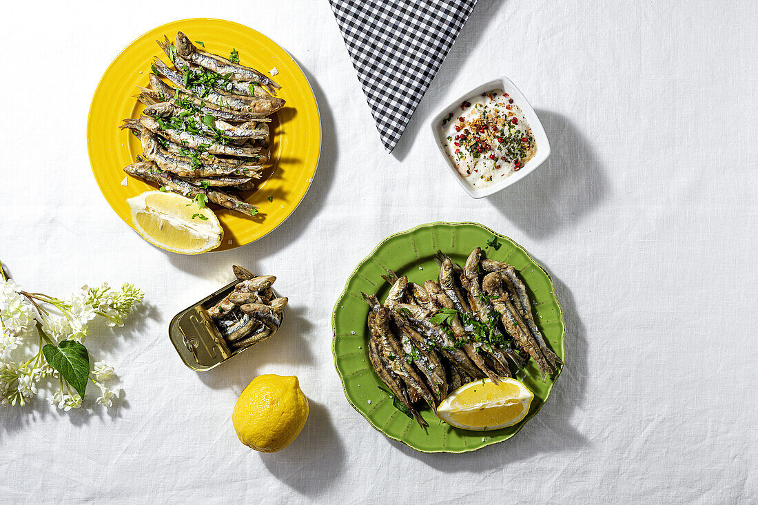 From above of fried and canned anchovies served on table with fresh lemons in restaurant in sunlight