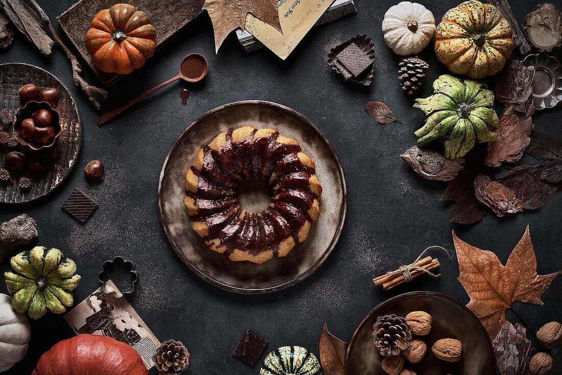 From above tasty appetizing pumpkin cake with chocolate cream on table decorated with autumn vegetables