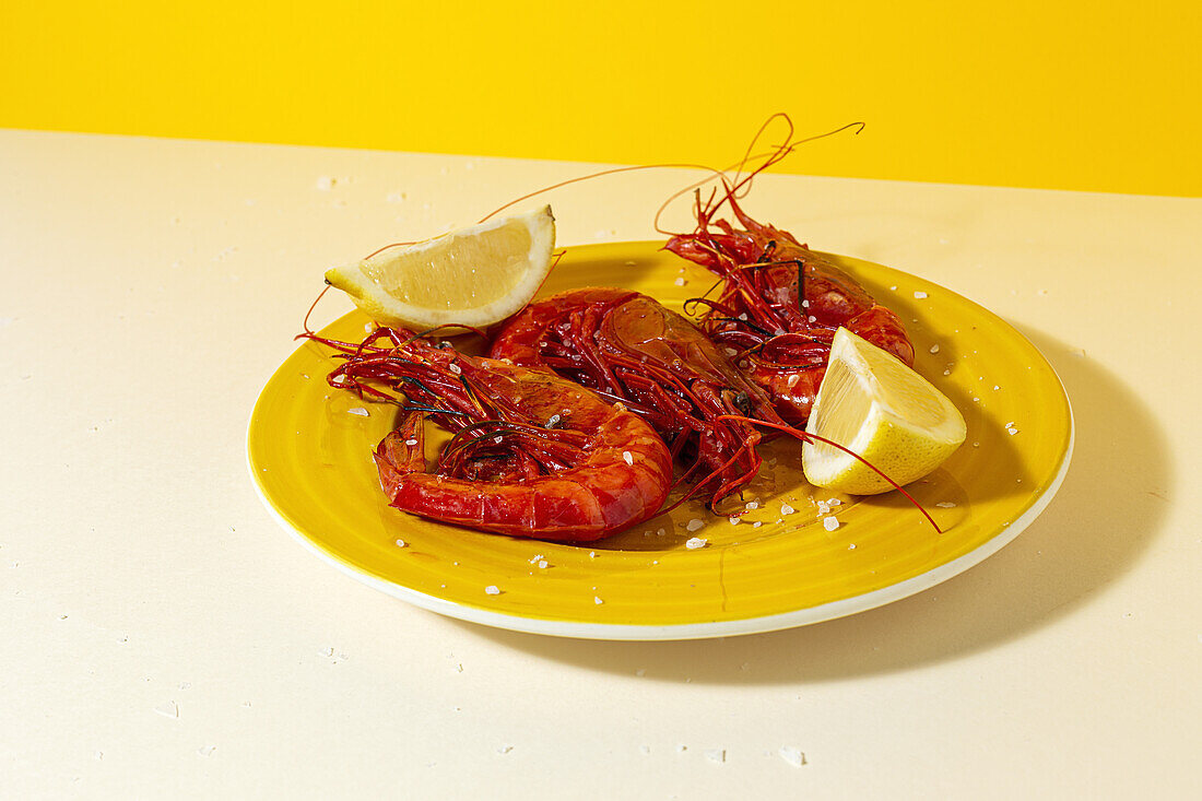 Tasty seafood of cooked red shrimps with fresh lemon slices and coarse salt on two color background