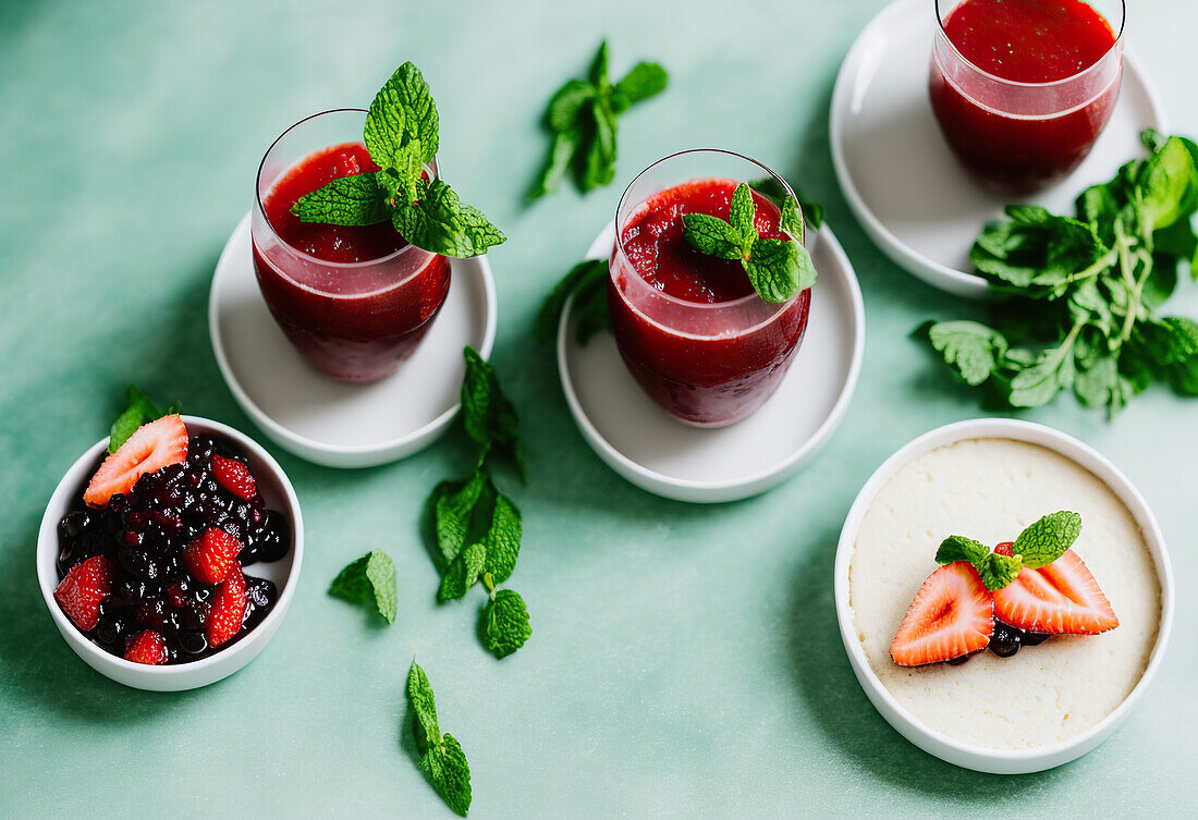 Hoher Blickwinkel auf leckere Smoothies mit Erdbeeren und Johannisbeeren, serviert in transparenten Gläsern mit Minzblättern