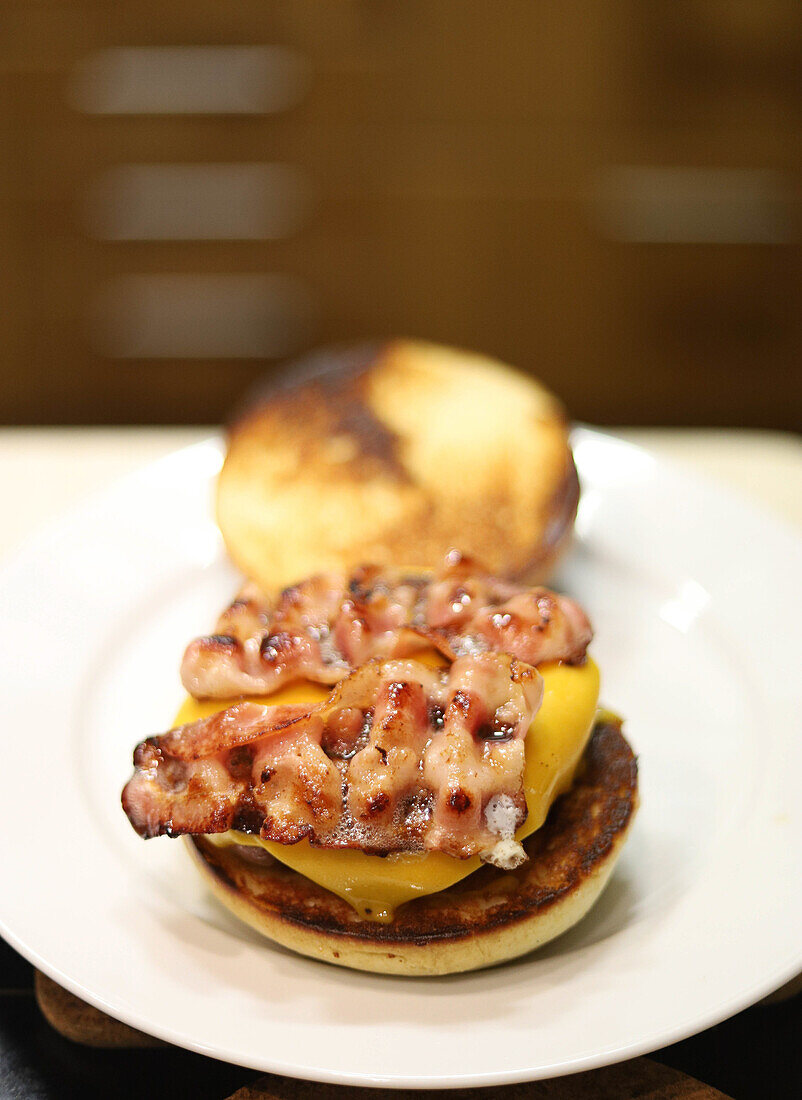 High angle of appetizing juicy hamburger with grilled bacon and cheese served on white plate placed on table