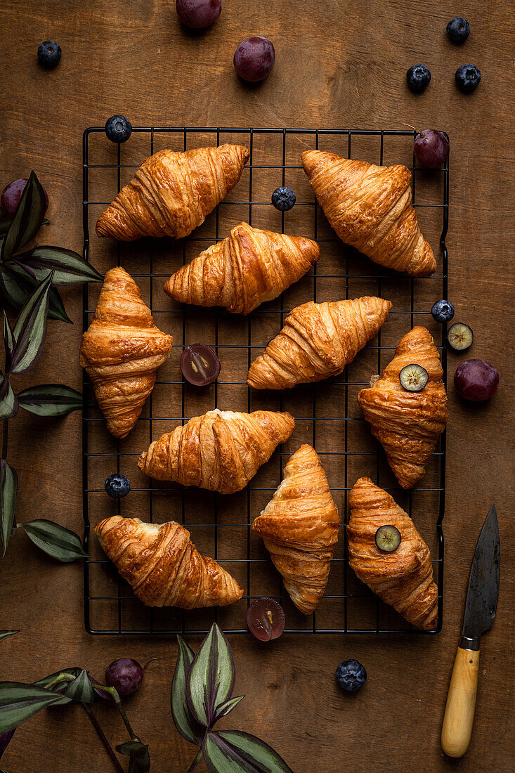 Blick von oben auf leckere süße, frisch gebackene Croissants mit Früchten auf einem Metallgitter auf einem Holztisch