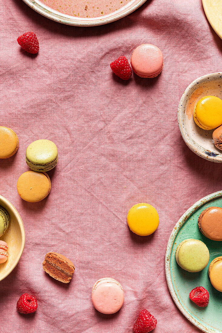 Ansicht von oben auf verschiedene runde Teller mit verschiedenen süßen, bunten französischen Makronen und Beeren auf rosa Tischtuch