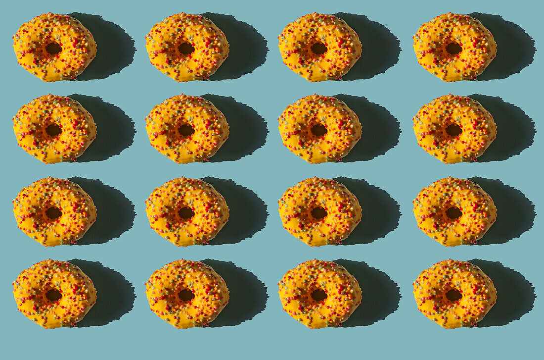 Top view of many donuts covered with yellow cover and colored balls on blue background