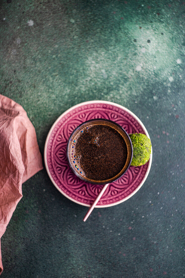 Blick von oben auf ein Glas türkischen Kaffee und traditionelle süße Pakhlava-Kugeln, serviert auf einem grünen Betontisch