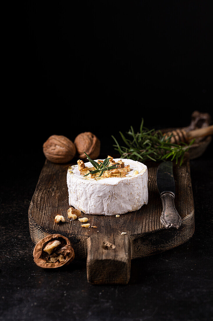Köstlicher Gourmet-Camembert-Käse, garniert mit Walnüssen und frischem Rosmarin, serviert auf einem rustikalen Holzbrett