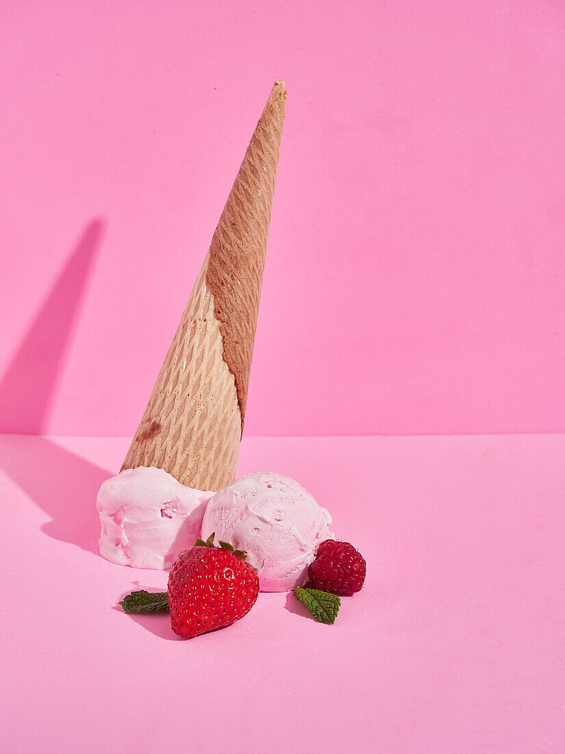Delicious sweet strawberry ice cream scoops with fallen crispy cones near ripe berries against pink background with shadow in studio