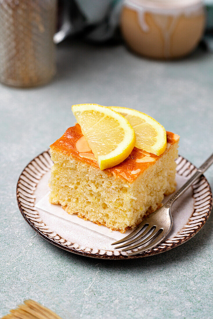 Square slice of delicious homemade lemon cake served on plate with fork on tray