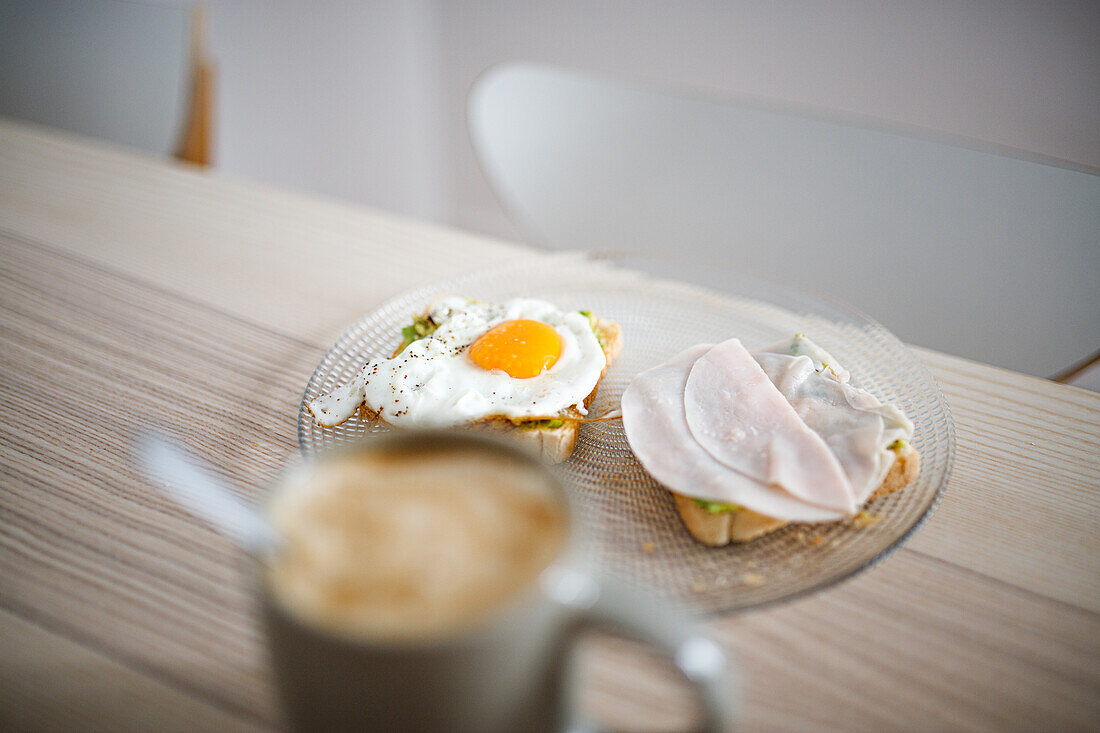 Hoher Blickwinkel auf leckere Sandwiches mit Spiegelei und Schinken auf einem Holztisch mit einer Tasse heißem Kaffee