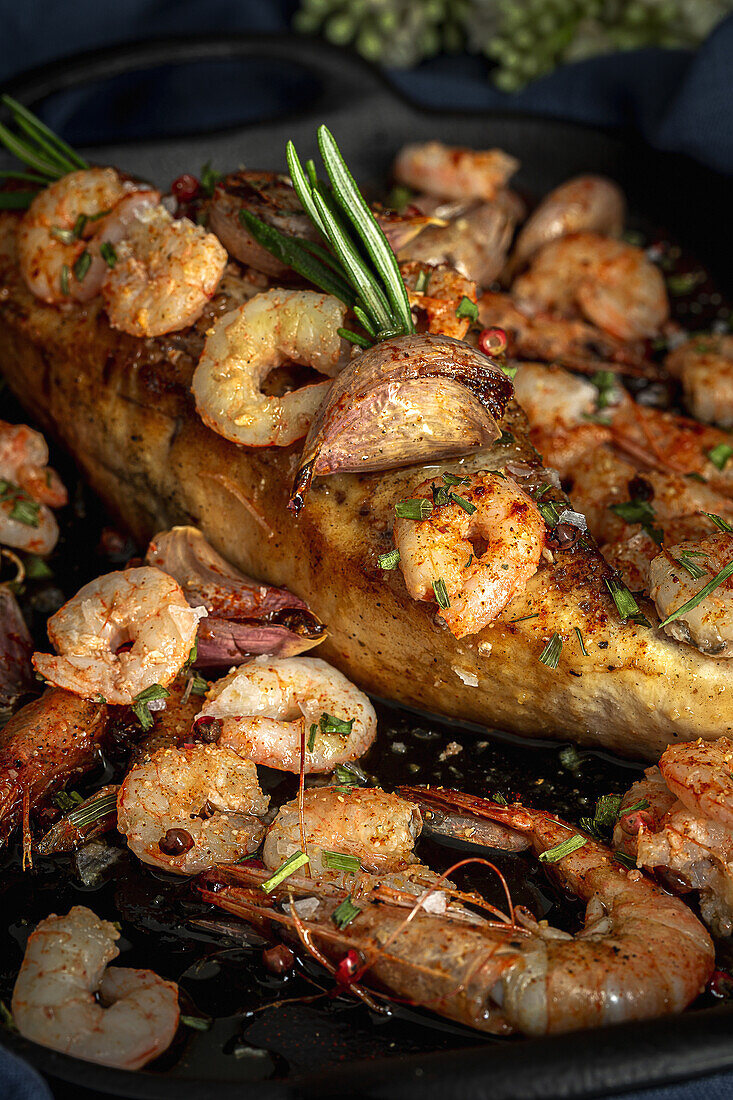 From above of black tray with appetizing baked swordfish served with prawns and confit garlic