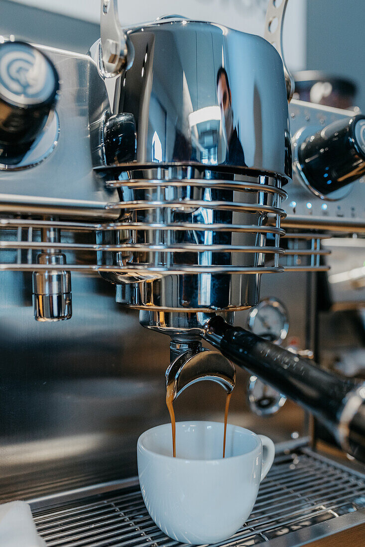 Modern professional coffee machine pouring fresh hot coffee into white cup in cafe in daytime