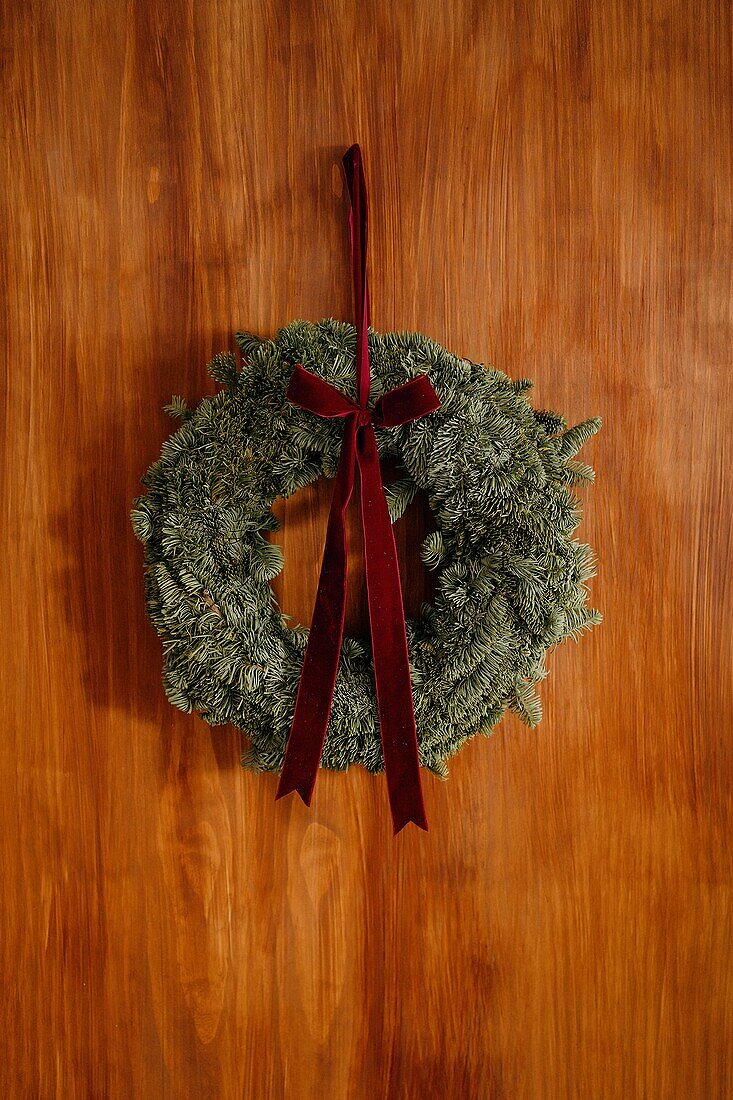 Dekorativer Nadelholzkranz mit roter Schleife, der in der Weihnachtszeit an einer Holzwand im Zimmer hängt