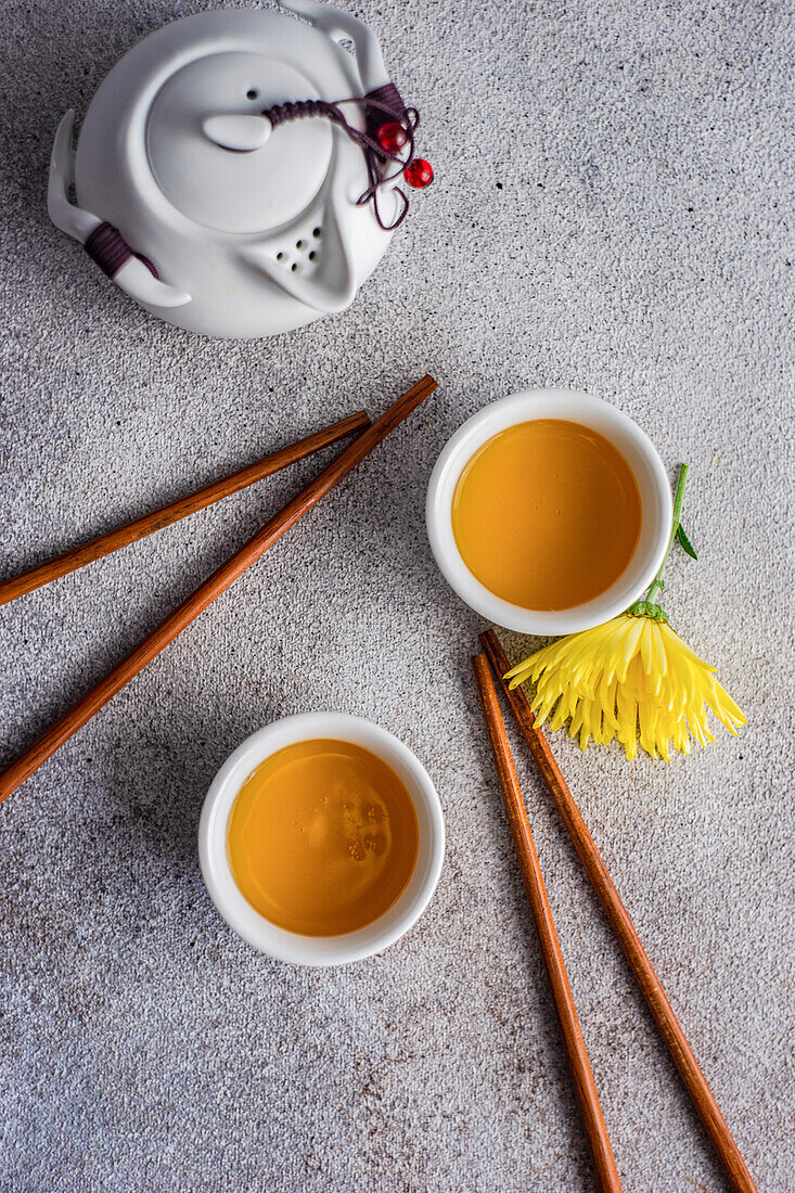 Draufsicht auf asiatisches Grüntee-Set mit gelben herbstlichen Chrysanth-Blüten, serviert auf Betontisch