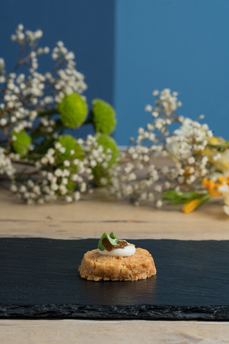 Single piece of delicious cooked appetizer bite served on black board near blooming white gypsophila near blue wall