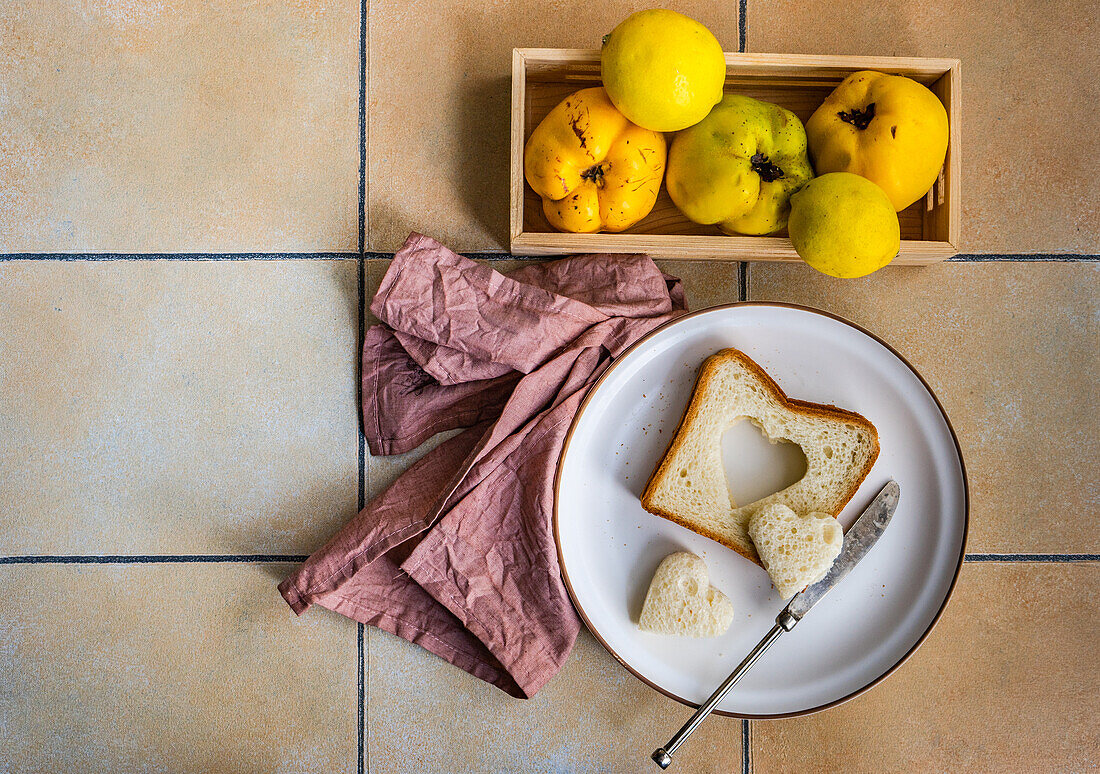 From above plate with toast slices and heart shaped cut and box with ripped quince fruit in wooden box